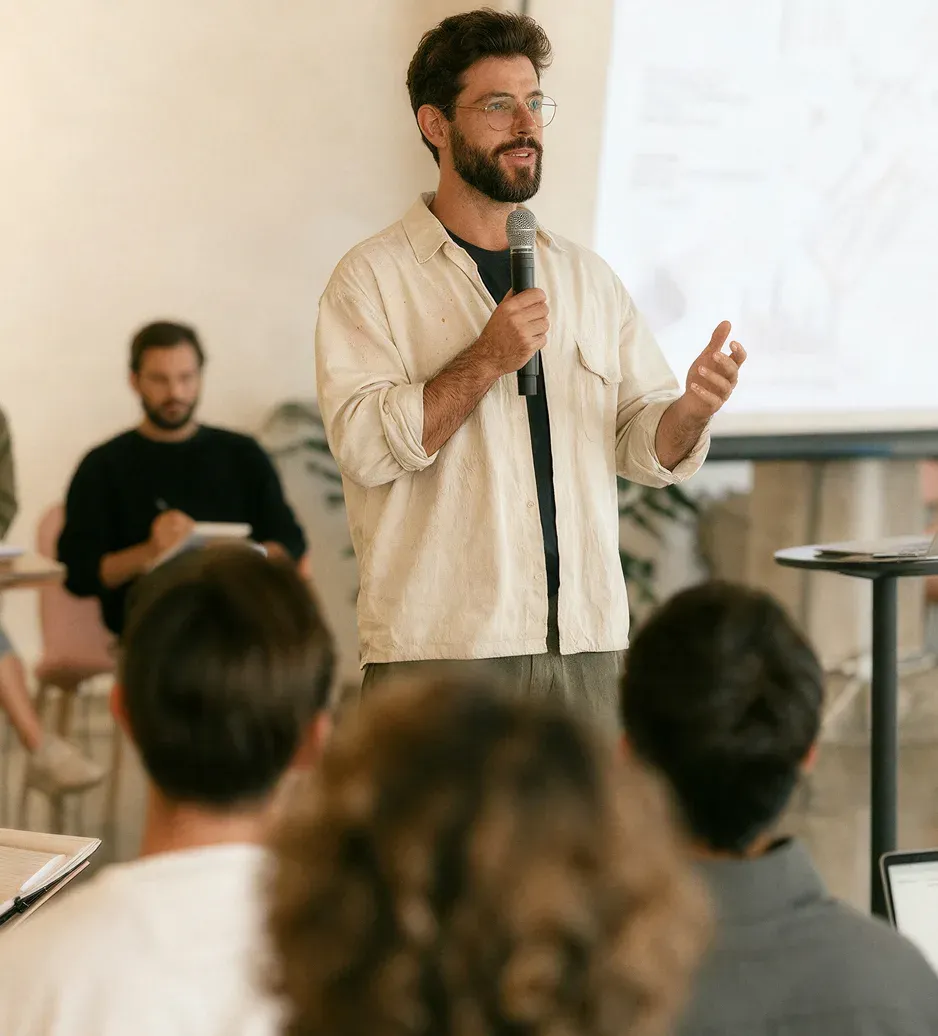 A speaker with a microphone presenting to founders at the Base44 Accelerator