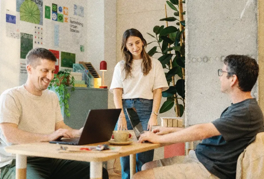 Three teammates working on laptops around a table