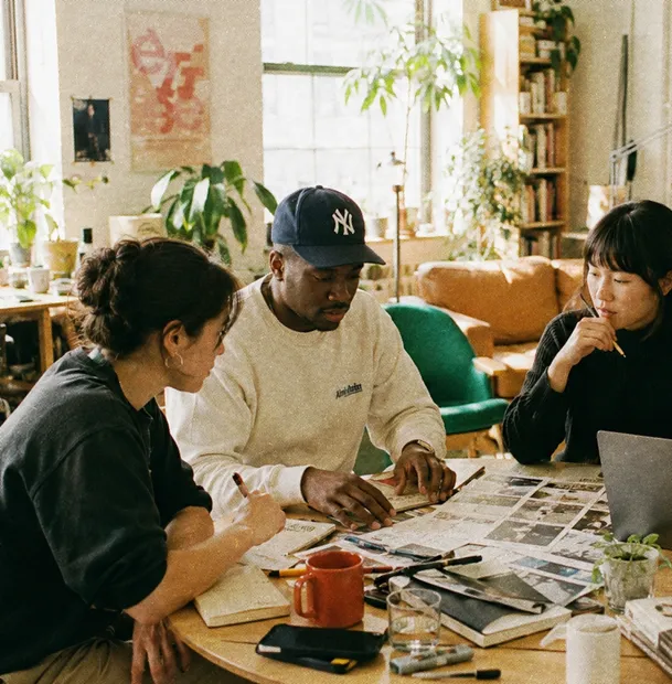 Four people working together at a table covered with laptops, papers and coffee cups