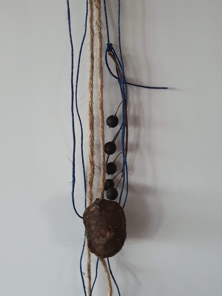 Dark seed pods and blue thread with rusty metal disc | תרמילי זרעים כהים וחוט כחול עם דיסק מתכת חלוד