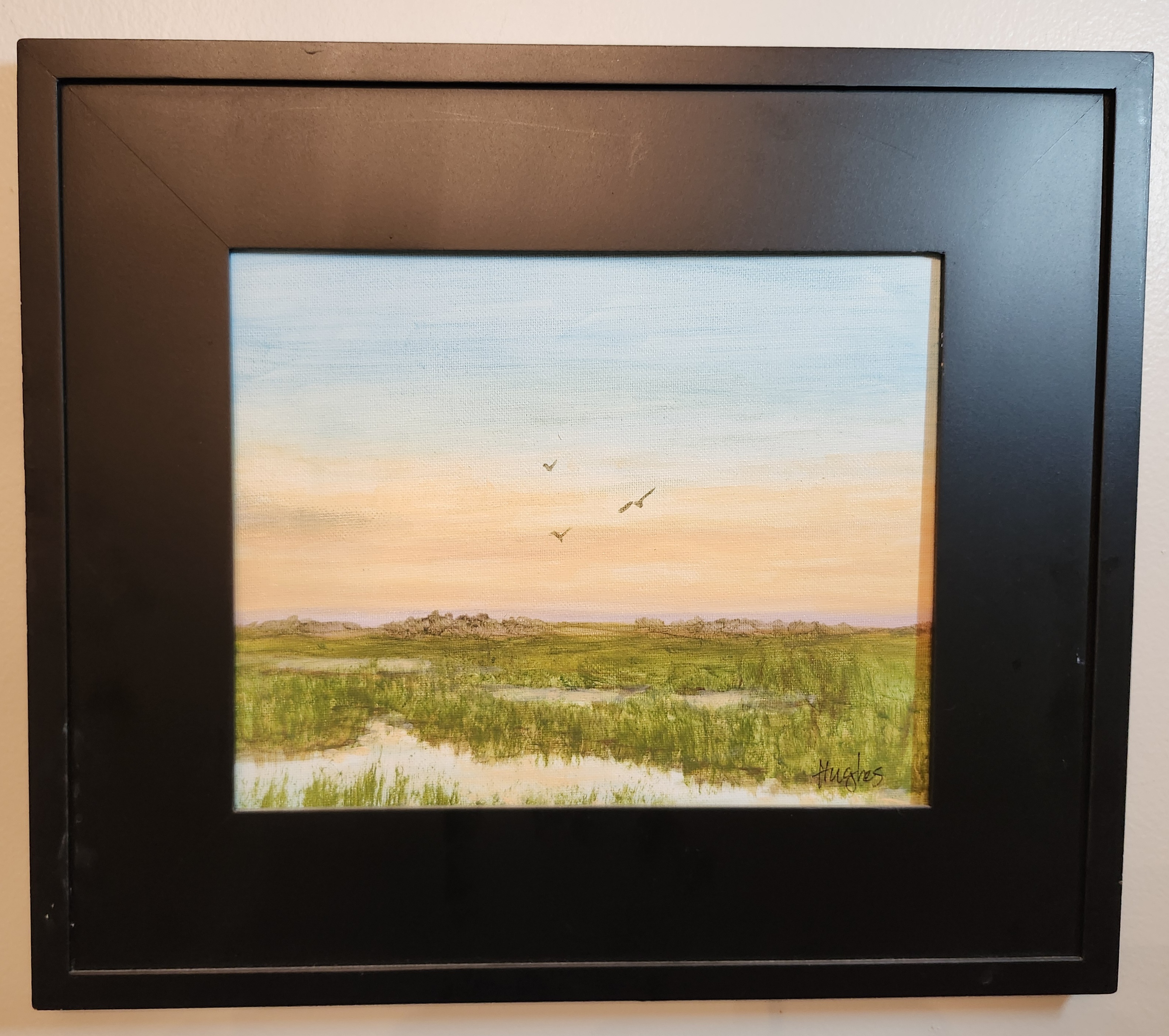 Serene coastal marsh at sunrise with a pale azure sky, peach-gold horizon, reflective pools and three small birds in flight.