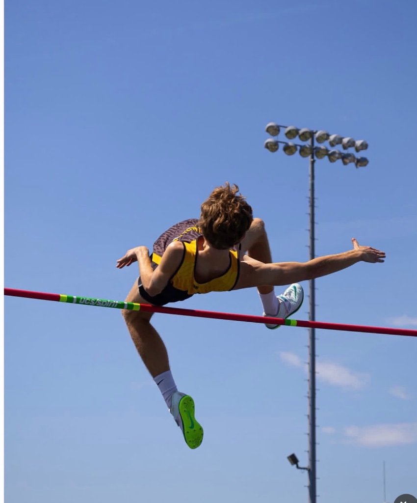 Wade Williams mid-flight clearing a high jump bar against the sky