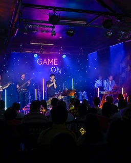 The full GAME ON line-up on stage in blue light