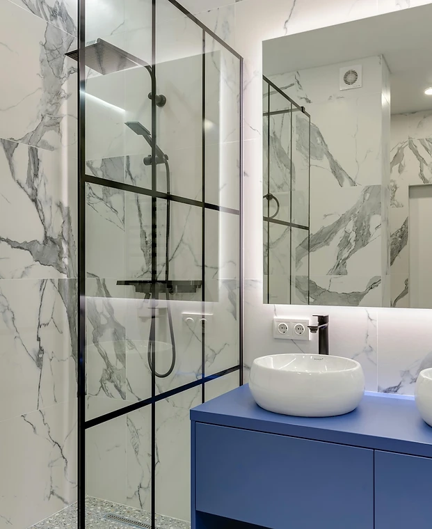 Salle de bain lumineuse, vasque blanche, meuble bleu et paroi de douche architecturale