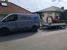 Simon-Firmenfahrzeug mit Anhänger und Minibagger vor einem Wohnhaus