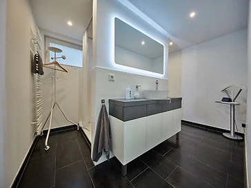 Fertig modernisiertes Bad mit beleuchtetem Spiegel und dunklem Fliesenboden