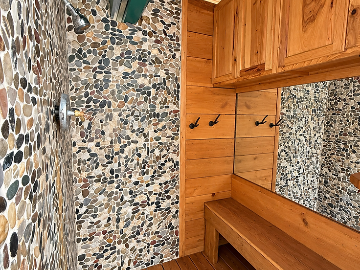 Private outdoor sauna room with a river-stone shower wall, knotty-pine wood bench and forest-green trim