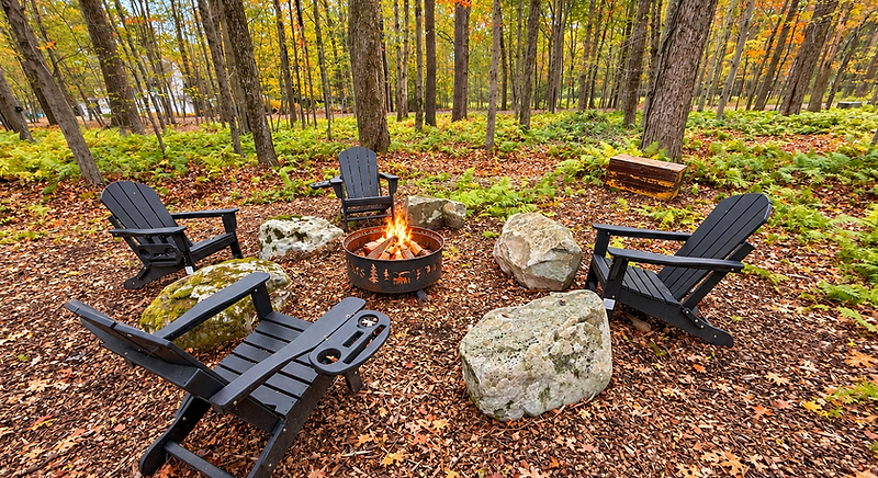 Backyard fire pit glowing with Adirondack chairs surrounded by autumn forest