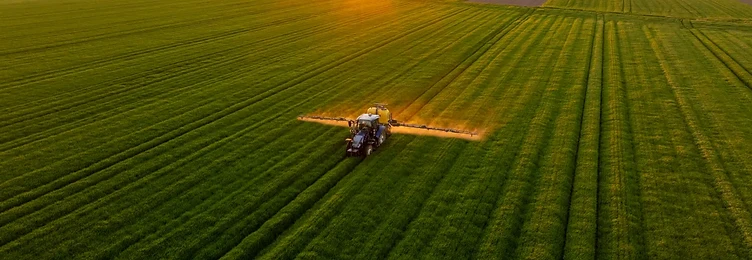 Tractor spraying crops at sunset
