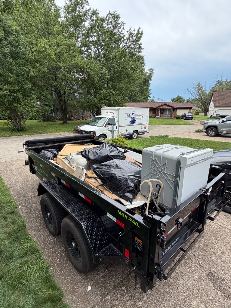 Dump trailer loaded with mixed debris and appliances in a neighborhood