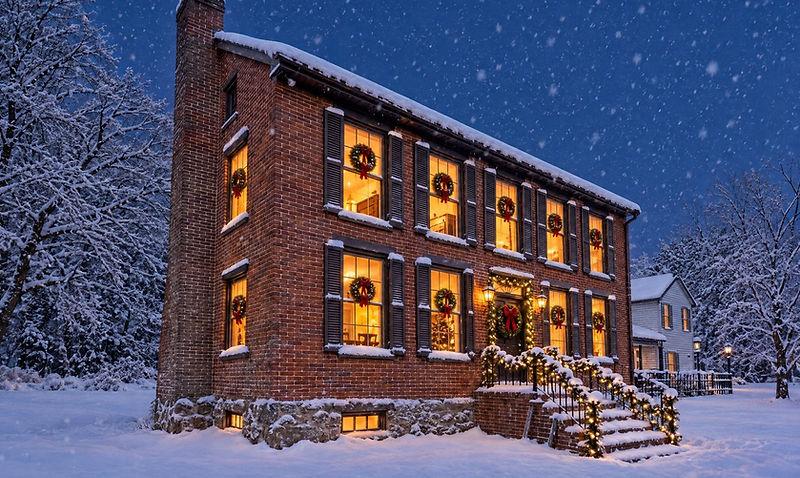 Wreath-lit windows and garland on a historic Gettysburg brick inn at dusk while snow falls