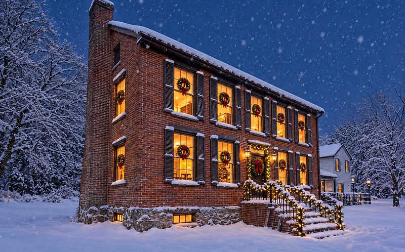 Baladerry Inn, a historic brick countryside inn near Gettysburg, with wreath-lit windows glowing in the snow at dusk
