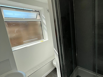 Bathroom after: dark-panelled shower, grey wood-effect flooring and white basin