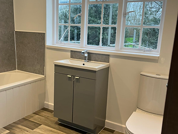 Bathroom finished: grey cabinetry, white bath and wood-effect flooring