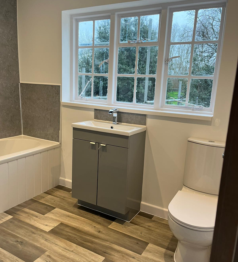 Bathroom finished: grey cabinetry, white bath and wood-effect flooring