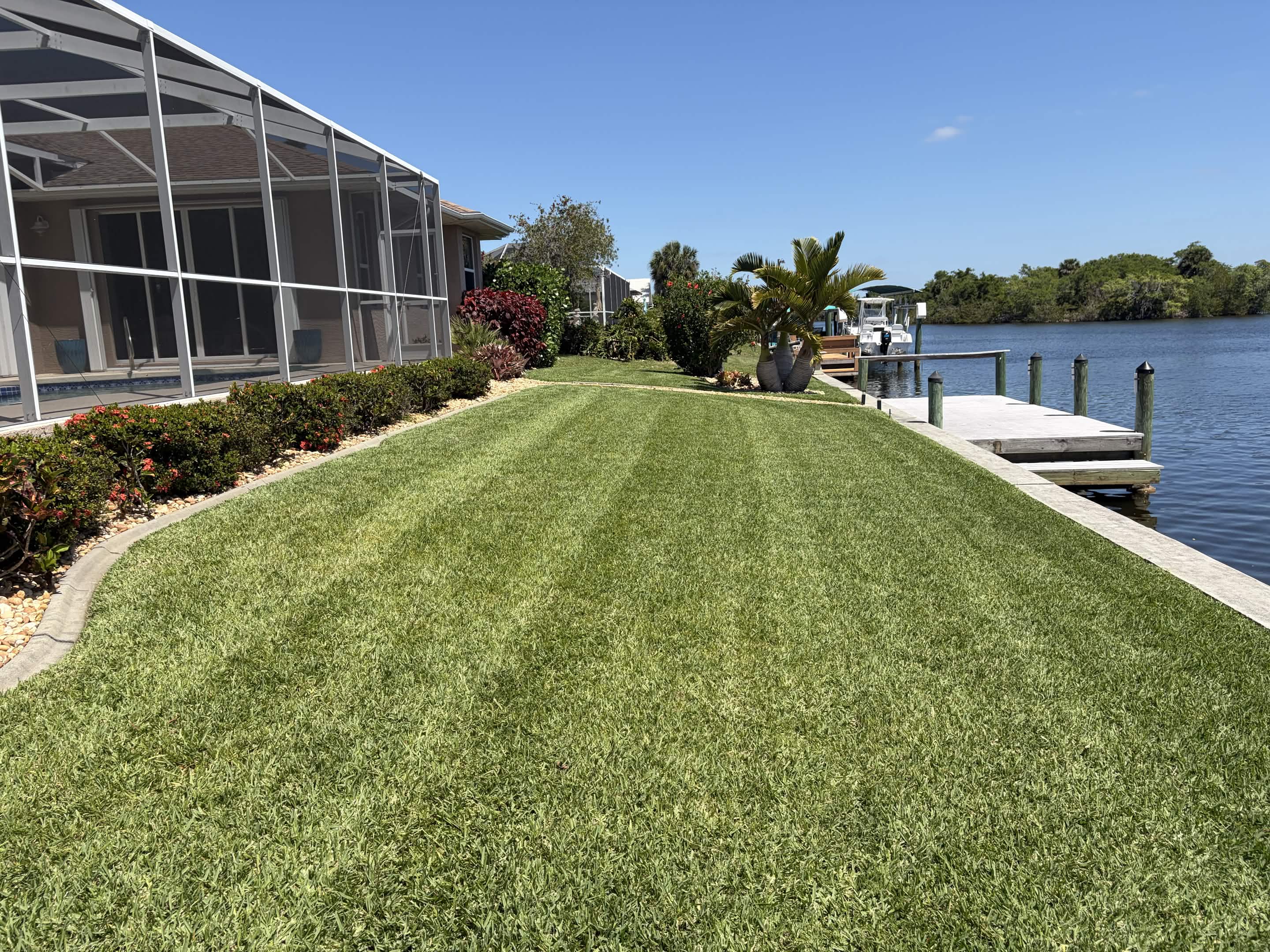 Waterfront property with precision-striped lawn and manicured hedge borders