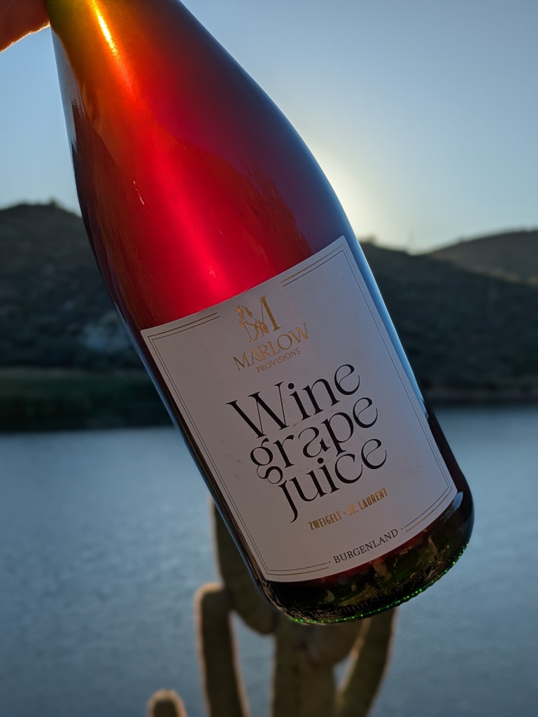 Marlow Provisions Wine Grape Juice bottle held at sunset over a lake