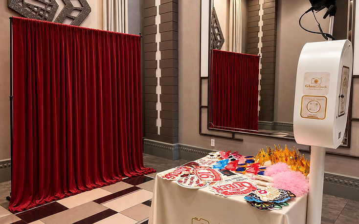 GlamBooth premium photo booth setup with red backdrop, professional lighting and prop table