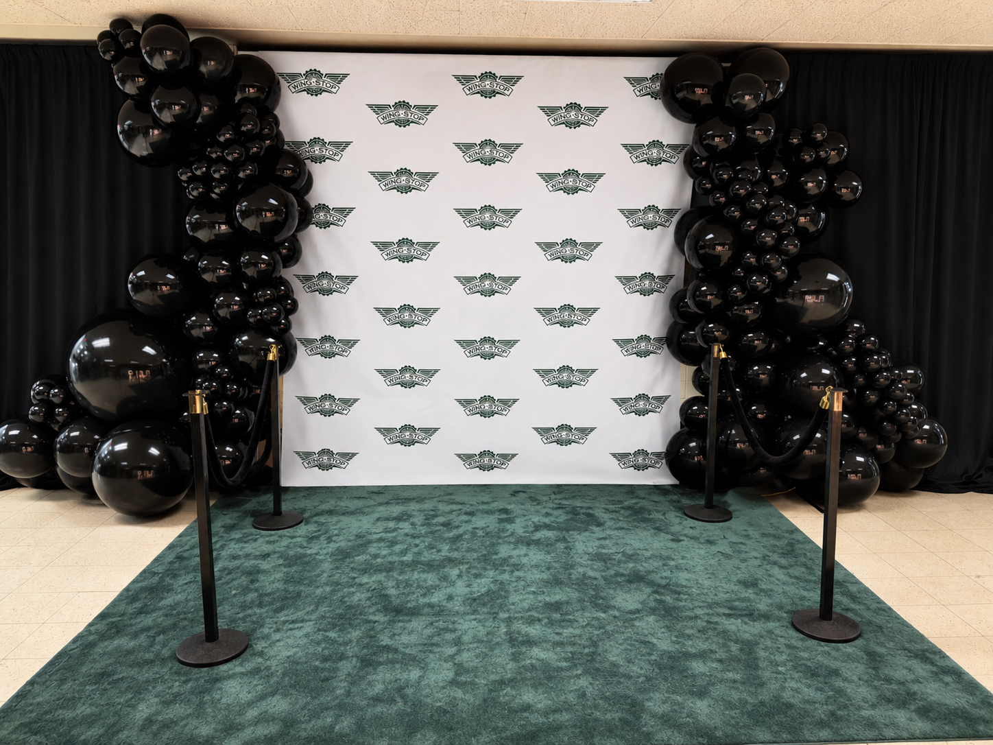 Offscript grand opening step-and-repeat event backdrop with black balloon garlands and emerald carpet