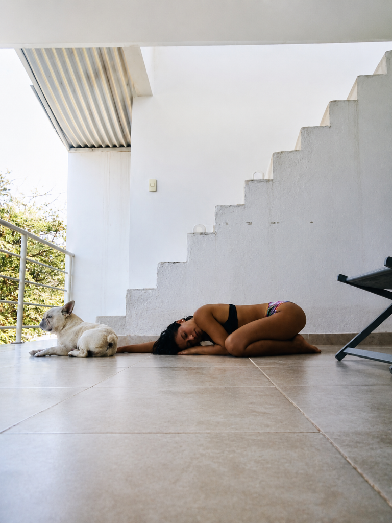 Nikki resting peacefully beside her French Bulldog in a sun-drenched white plaster space, a moment of quiet companionship
