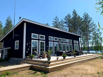 Färdigbyggt bostadshus med mörk träfasad, stora fönsterpartier och trädäck.