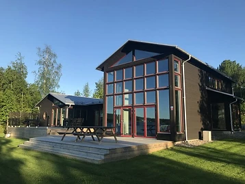 Modern villa med svartmålad träpanel, röda fönsterbågar och flernivåträdäck.