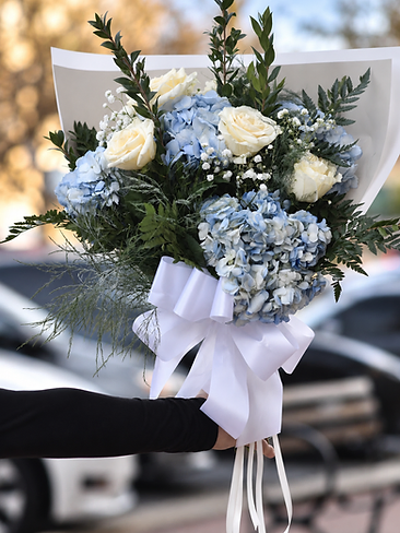 Hand-held bouquet of light blue hydrangeas and white roses tied with a white ribbon