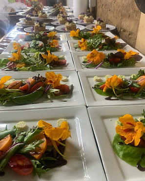 Rows of white rectangular plates with green salads topped with orange nasturtium flowers, with more plated starters lined up behind them