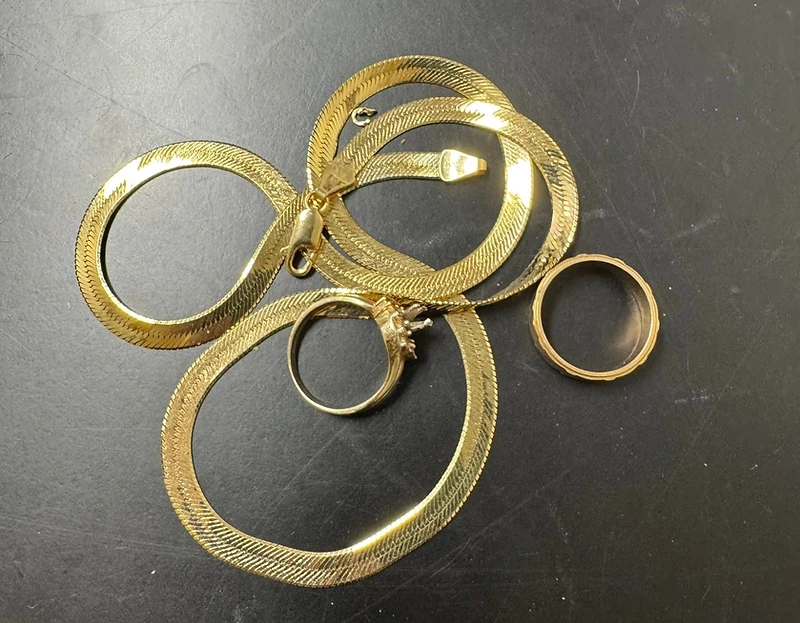 Gold herringbone chains and rings on a dark evaluation surface at Gold Pros