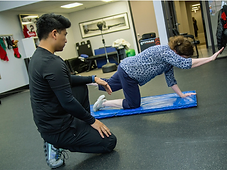 Migma Tamang coaching a client through a controlled bird-dog movement on a training mat.