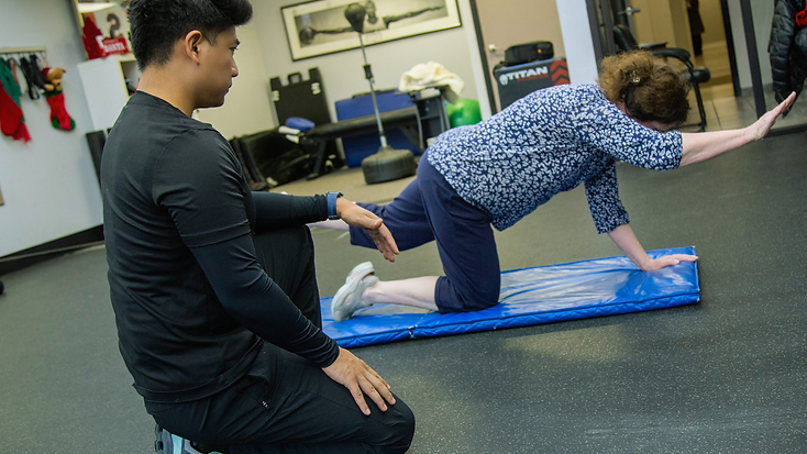 Migma Tamang coaching a client through a controlled bird-dog movement on a training mat.
