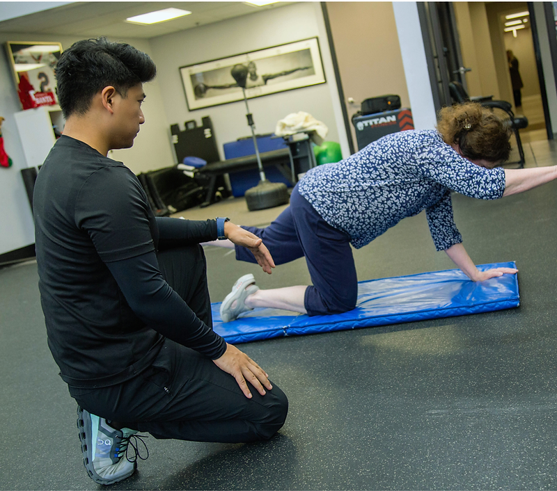 Migma Tamang coaching a client through a controlled bird-dog movement on a training mat.