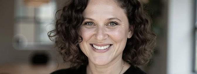 Portrait of Lisa Sledd, LMFT, a woman with curly shoulder-length brown hair smiling warmly, wearing a black top.