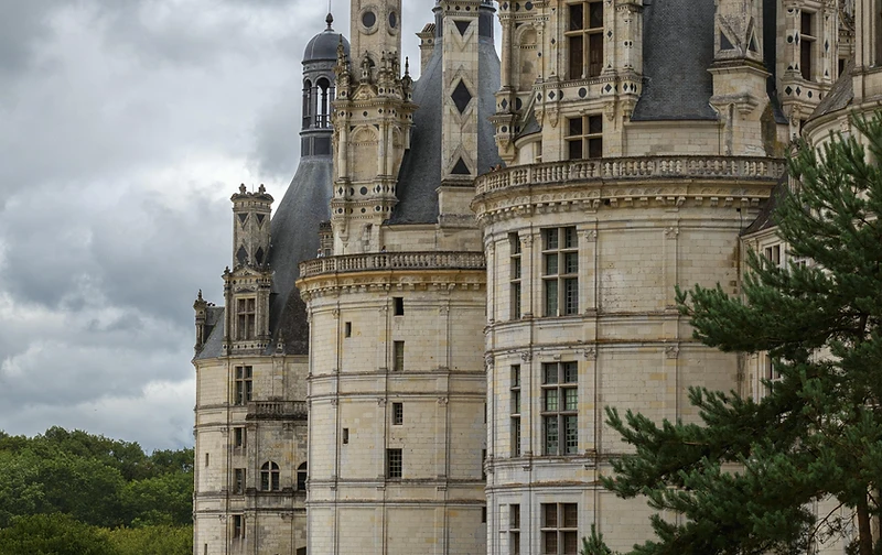 A vast historic chateau beneath heavy grey clouds — grandeur, scale, and old-world exclusivity