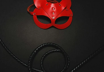 Red leather feline mask with silver rivets laid over a coiled black whip