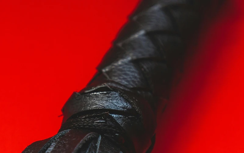 Braided black leather flogger handle photographed against saturated crimson red