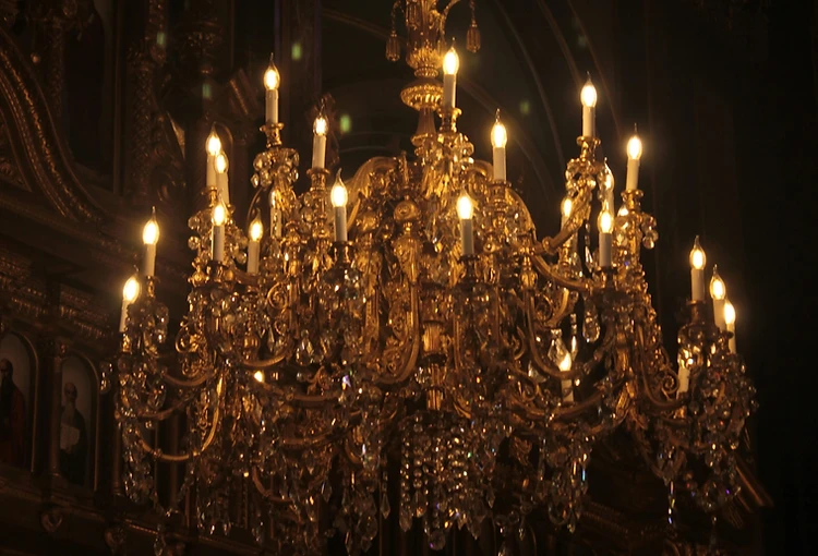 Antique gold crystal chandelier glowing against near-total darkness in a private salon