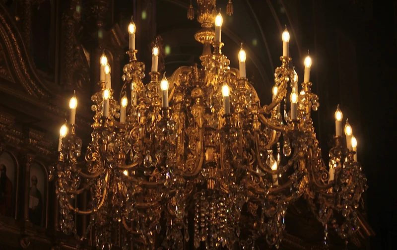 An ornate antique-gold crystal chandelier glowing warmly against near-total blackness
