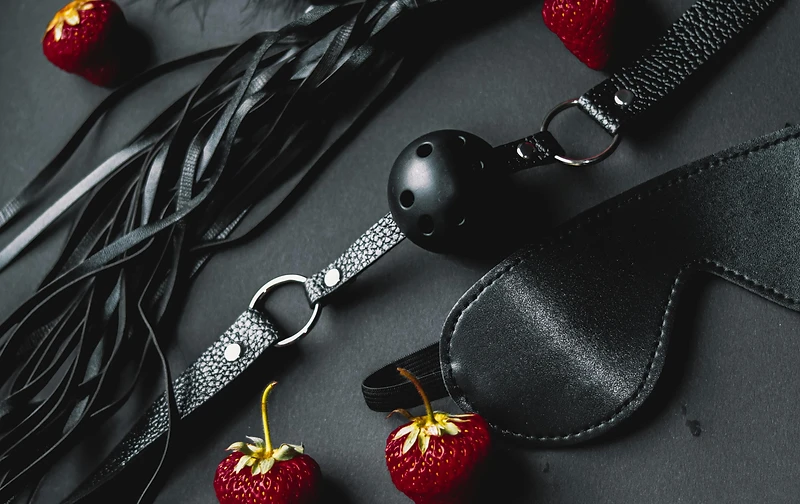 Black leather implements with red strawberries arranged on matte black — luxury boudoir still life