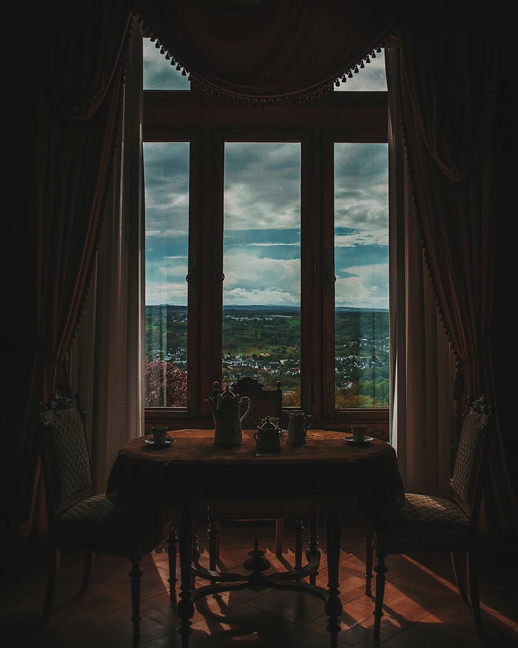 A private salon set for two, heavy drapes framing a window of pale daylight