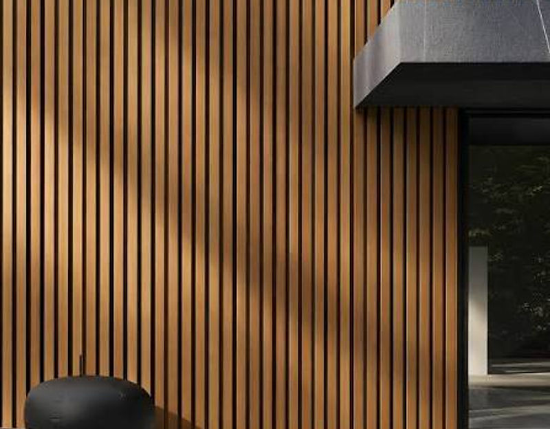 Facade of vertical wood cladding boards with a dark roof overhang and a light-toned deck