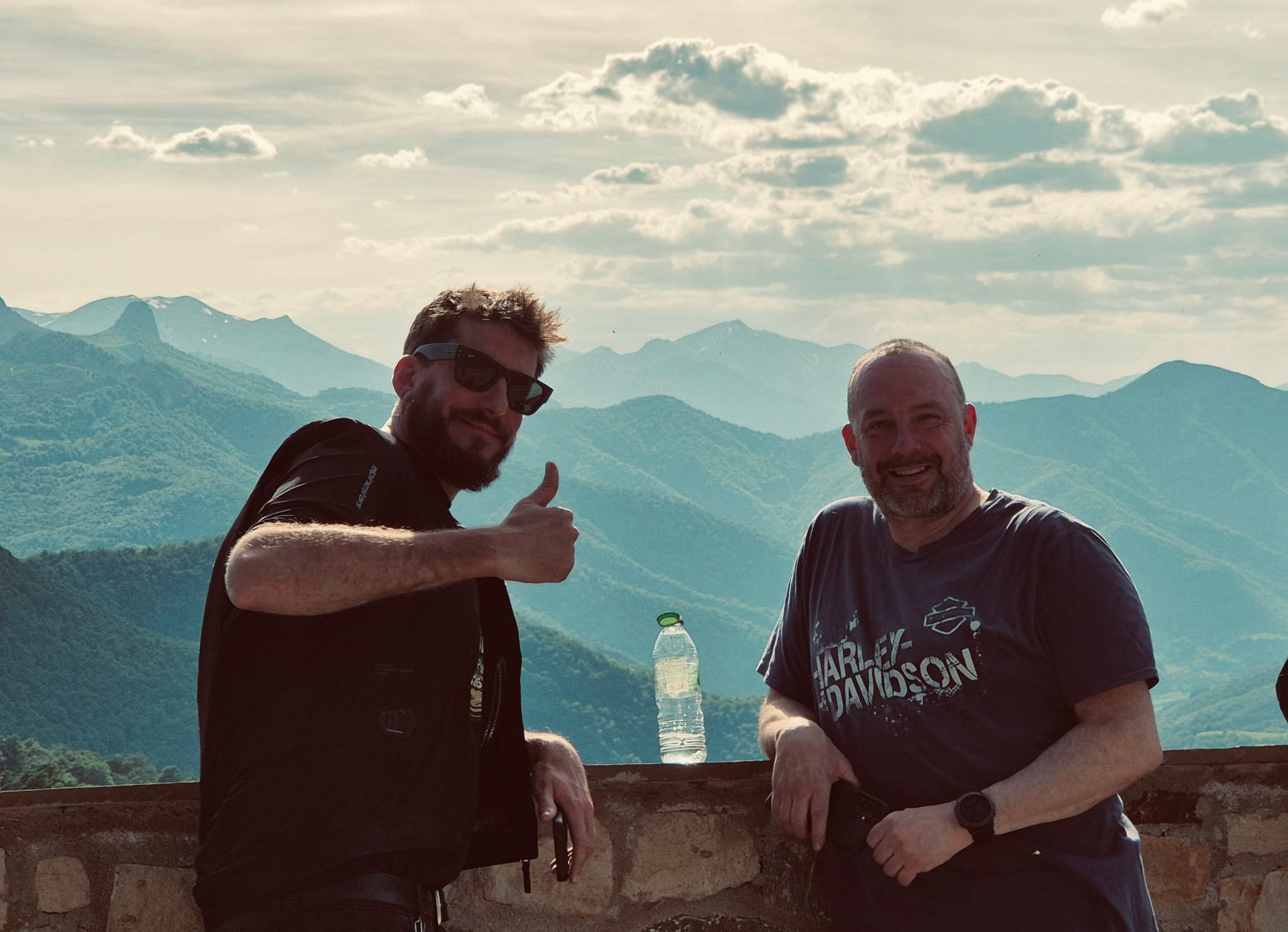 Two riders grinning at a mountain viewpoint with layers of Cantabrian mountains behind them