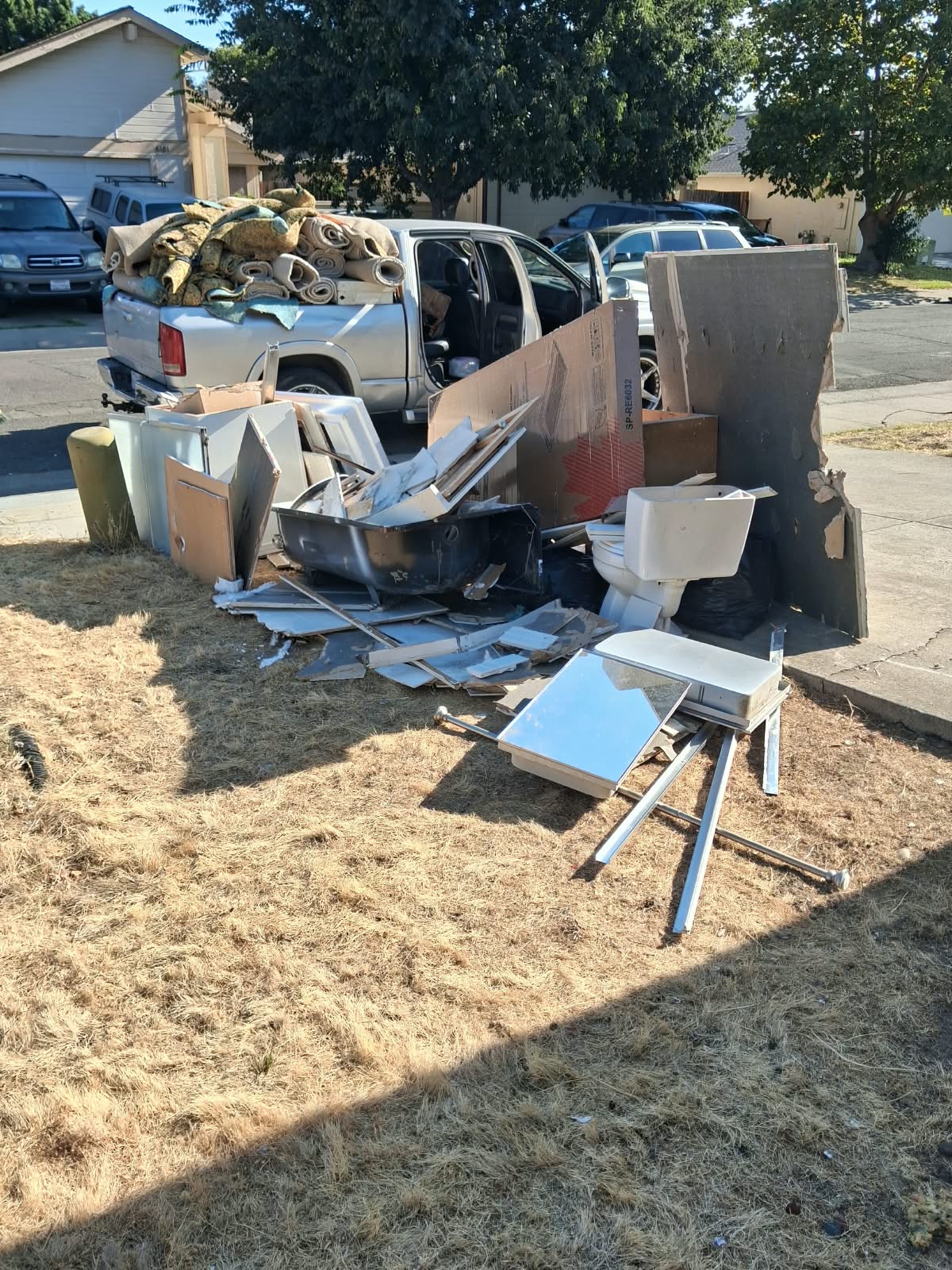 Complete clean-out load — carpet rolls, kitchen cabinets, sink, and construction debris staged curbside for dump hauling.